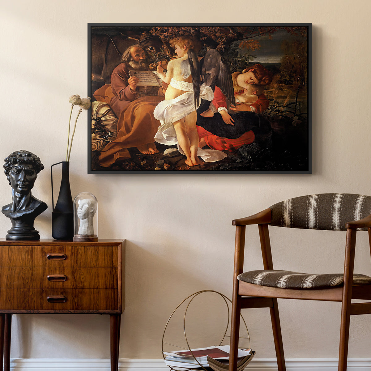 Rest on the Flight into Egypt, c. 1597 by Caravaggio as a black floater framed canvas featuring a peaceful religious moment with figures reclining in natural setting, styled above a mid-century console in a contemporary living area.