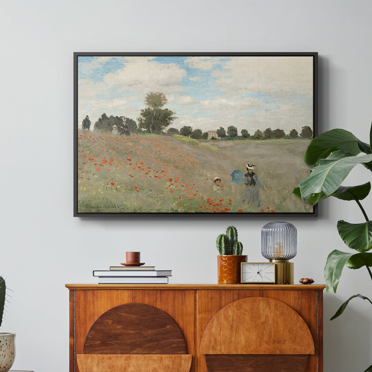 The Poppy Field near Argenteuil, 1873 by Claude Monet in a black floater framed canvas featuring a field of red poppies with figures walking across rolling landscape, displayed above a wood console cabinet.