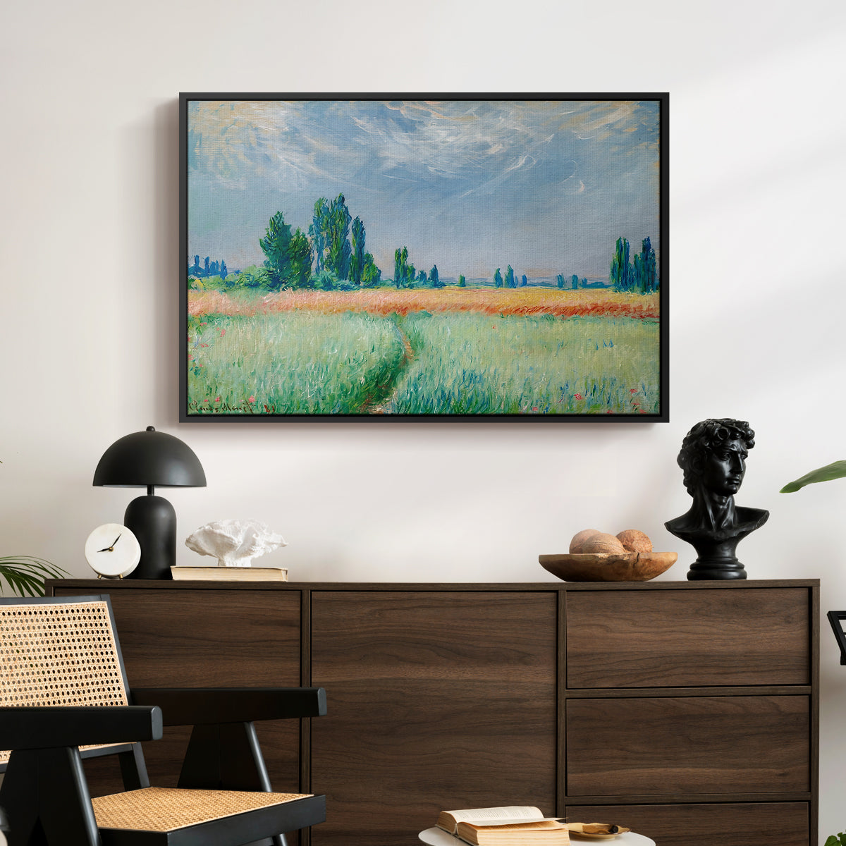 The Wheat Field (Champ de Blé), 1881 by Claude Monet displayed in a black floater framed canvas above a dark wood credenza in an entryway.