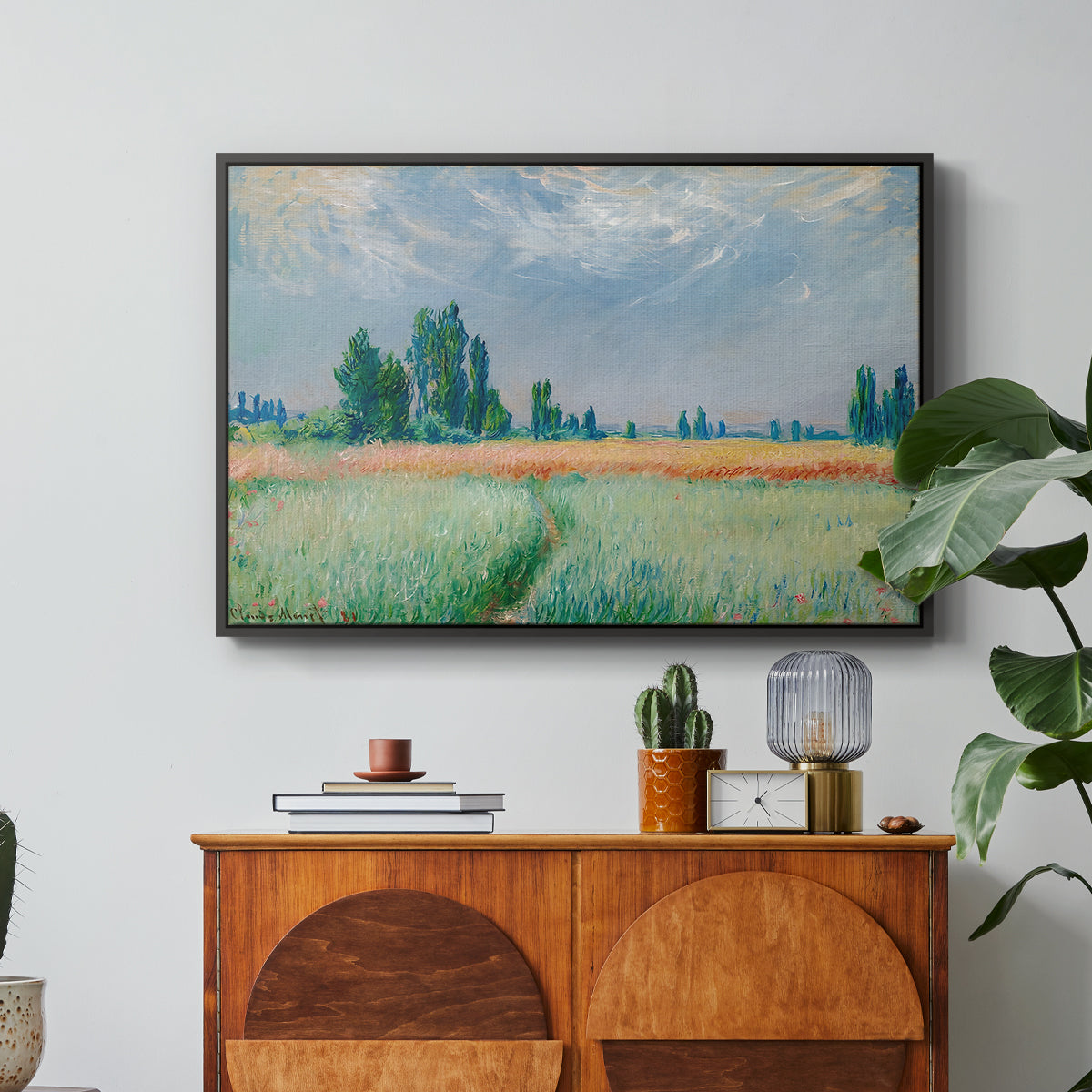 The Wheat Field (Champ de Blé), 1881 by Claude Monet in a black floater framed canvas featuring a golden wheat field stretching across landscape under soft sky, displayed above a wood console cabinet.