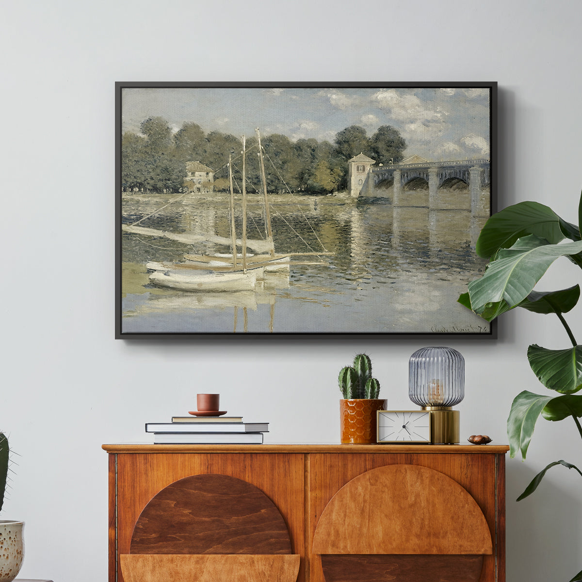 The Bridge at Argenteuil, 1874 by Claude Monet in a black floater framed canvas featuring a bridge spanning river with sailboats and reflections in water, displayed above a wood console cabinet.