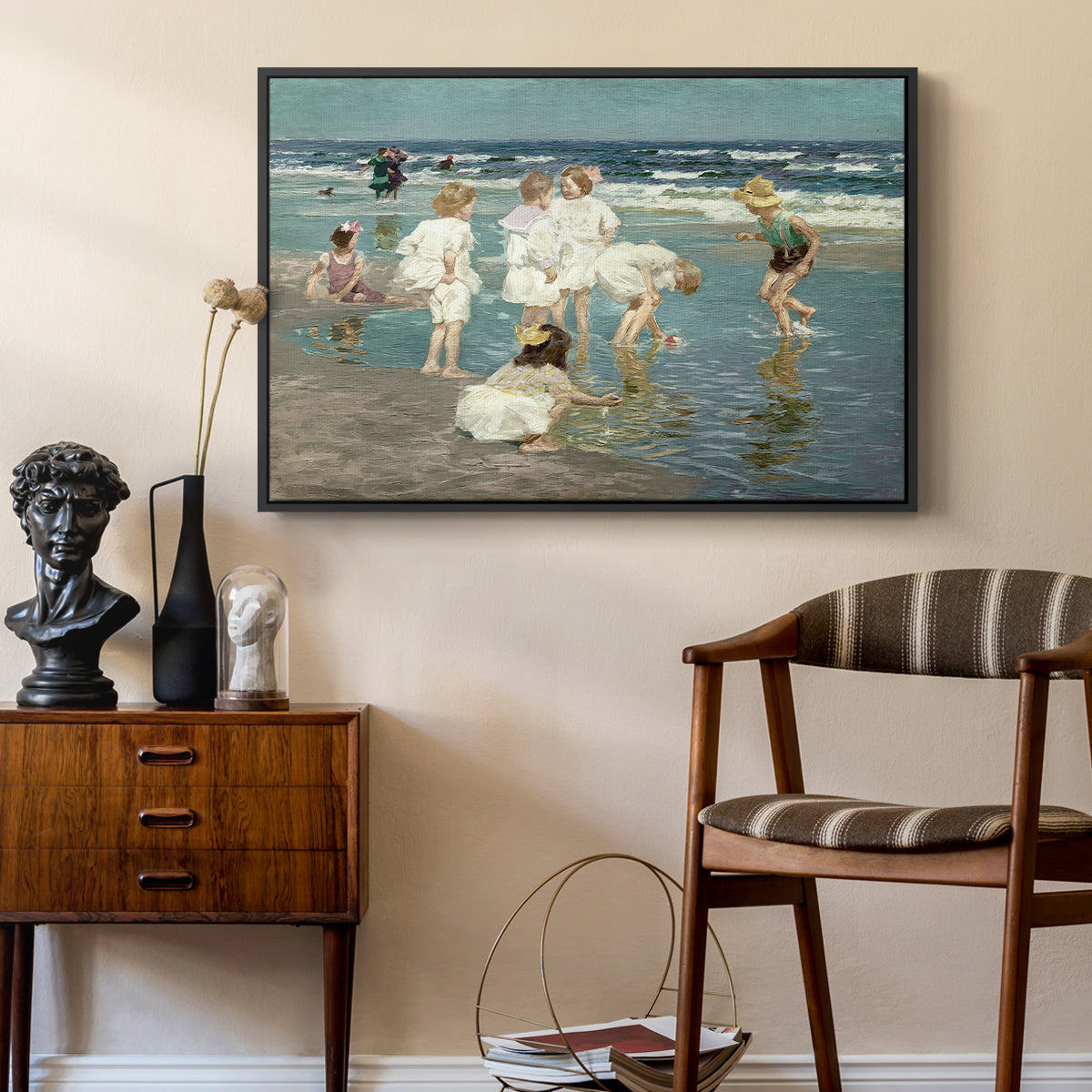 A Holiday, c. 1915 by Edward Henry Potthast as a black floater framed canvas featuring an impressionist coastal view of families enjoying seaside water, styled above a mid-century console in a contemporary living area.