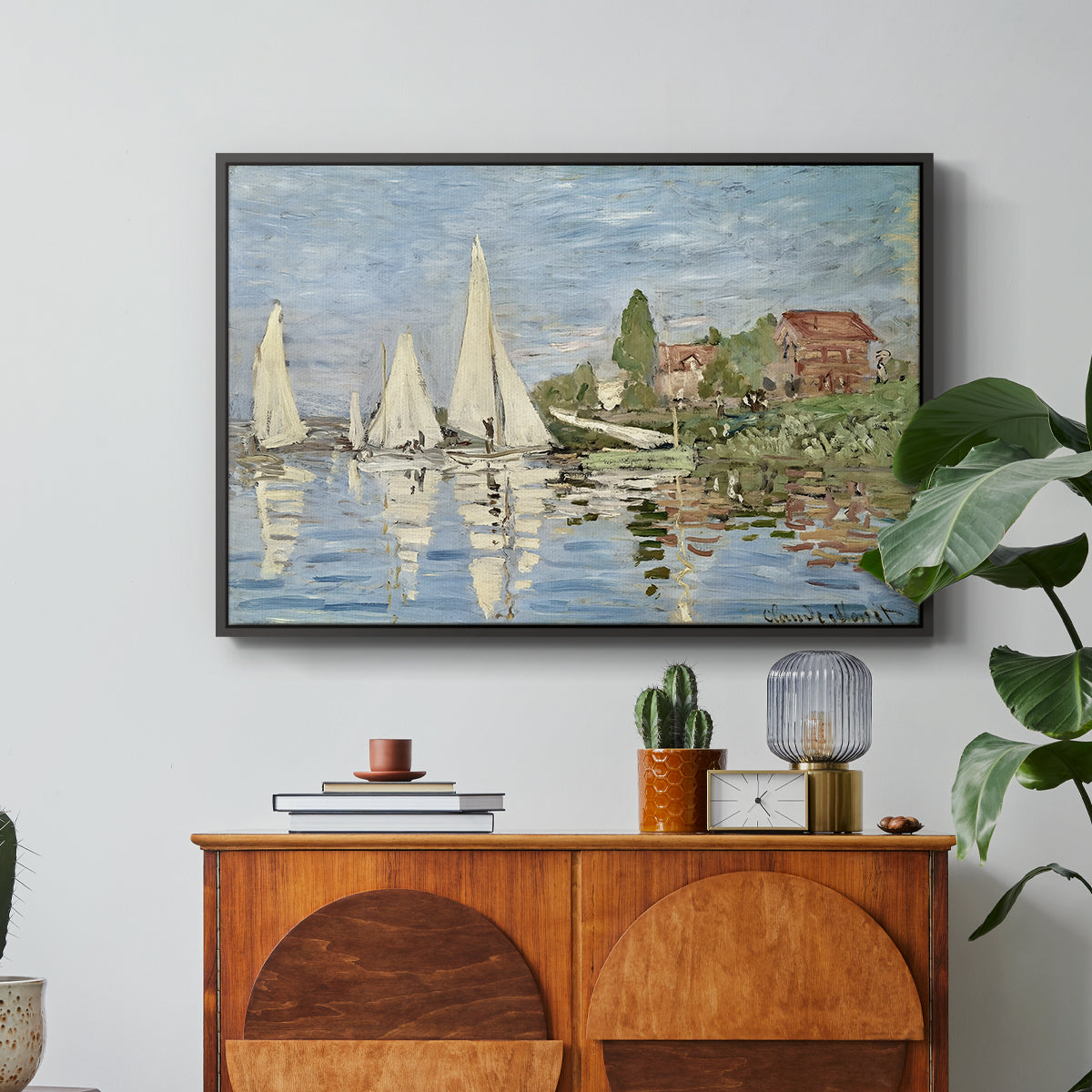 Regatta at Argenteuil, 1872 by Claude Monet in a black floater framed canvas featuring colorful sailboats racing across river under bright sky, displayed above a wood console cabinet.