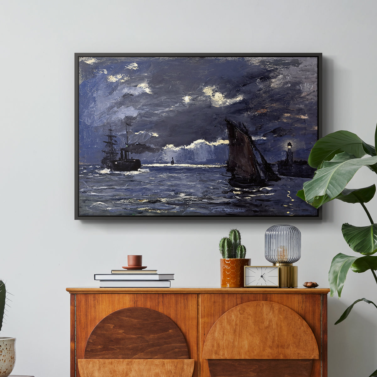 A Seascape, Shipping by Moonlight, 1864 by Claude Monet in a black floater framed canvas featuring ships on dark sea illuminated by moonlight under night sky, displayed above a wood console cabinet.