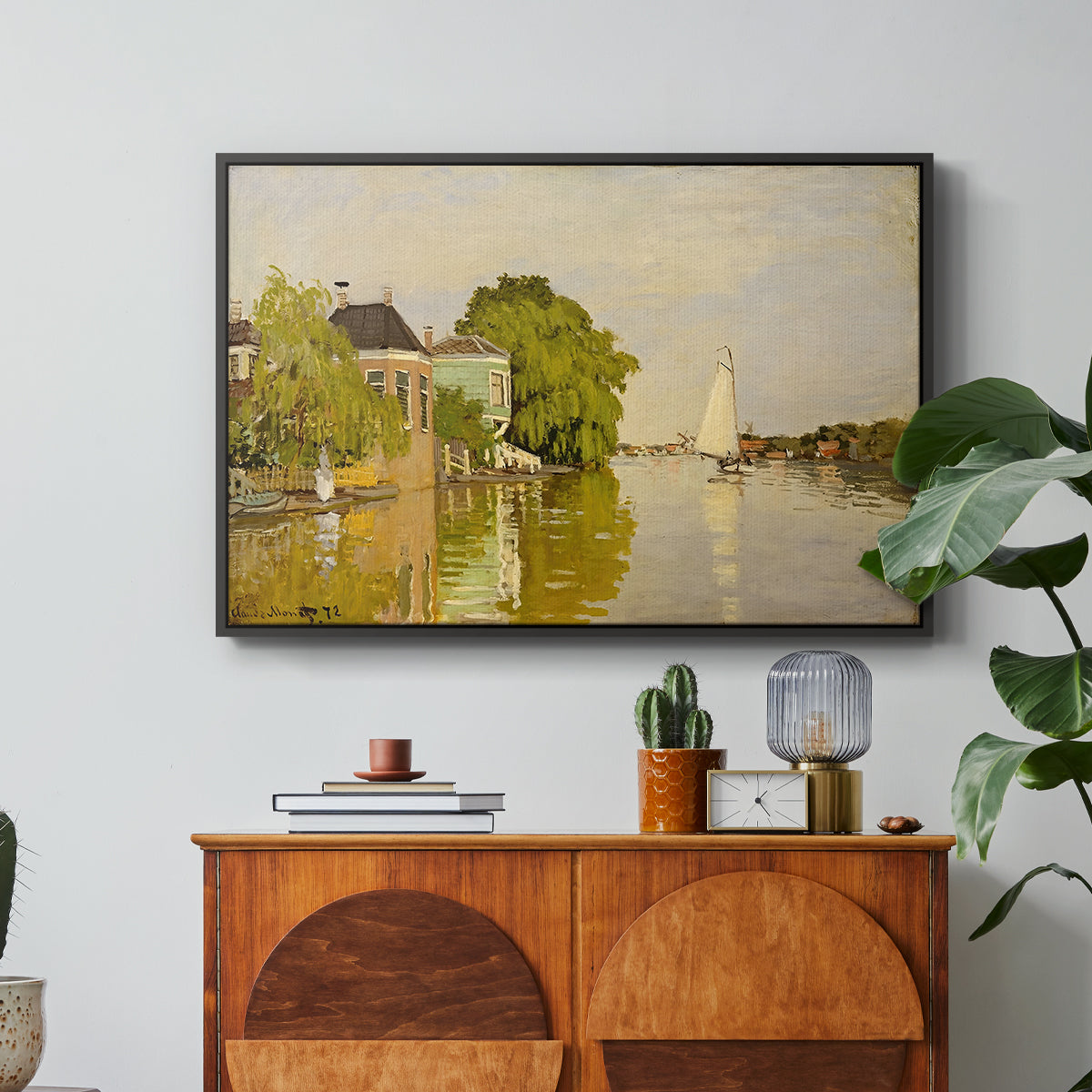 Houses on the Achterzaan, 1871 by Claude Monet in a black floater framed canvas featuring colorful houses reflected in calm river surrounded by greenery, displayed above a wood console cabinet.