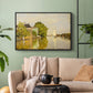 Black floater framed canvas featuring a peaceful village scene with houses bordering water, displayed above a sofa in a modern living room.