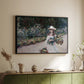 Black floater framed canvas of Young Girl in the Garden at Giverny, 1888 by Claude Monet, featuring an impressionist garden scene with child among greenery and blossoms above a sideboard in a softly lit hallway.