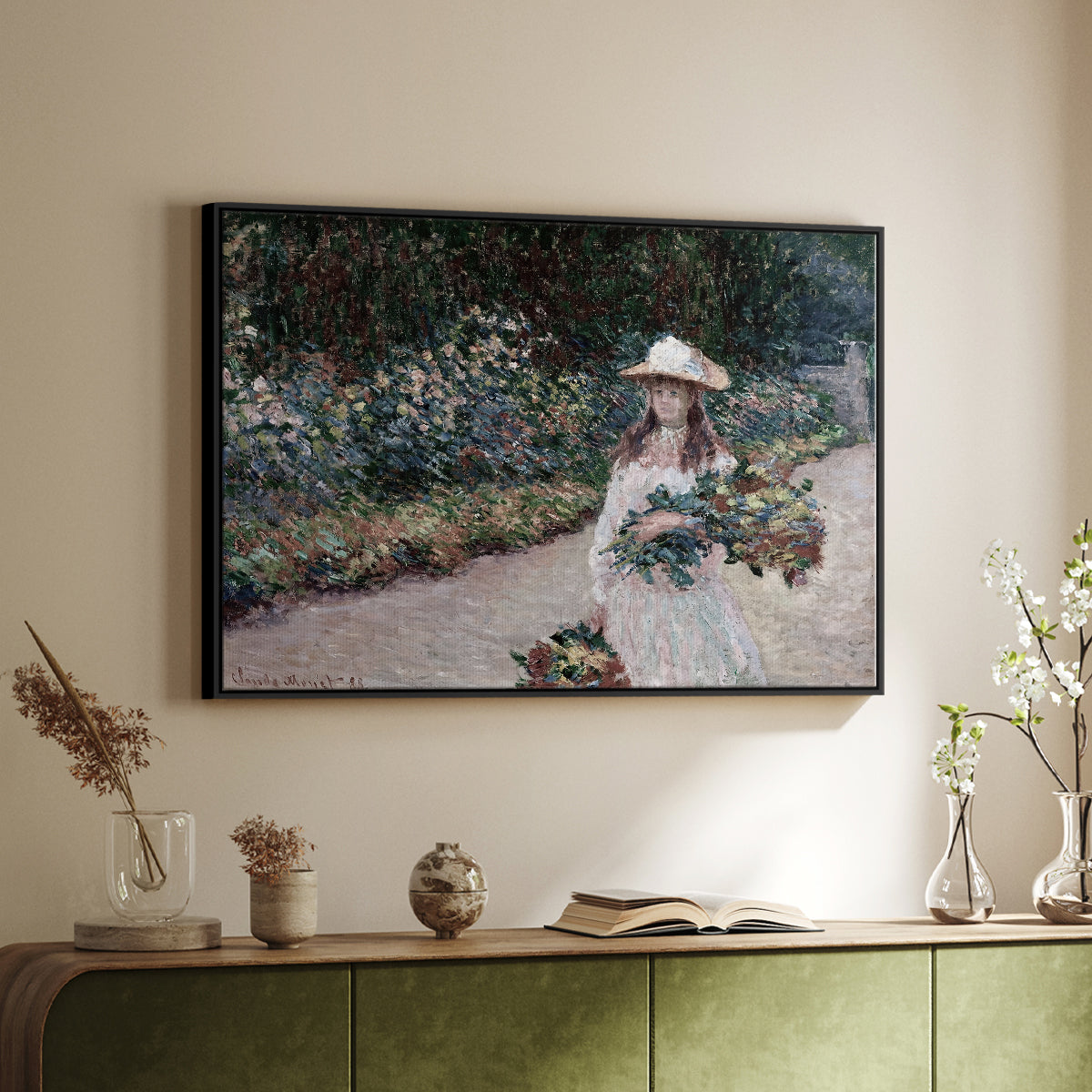 Black floater framed canvas of Young Girl in the Garden at Giverny, 1888 by Claude Monet, featuring an impressionist garden scene with child among greenery and blossoms above a sideboard in a softly lit hallway.