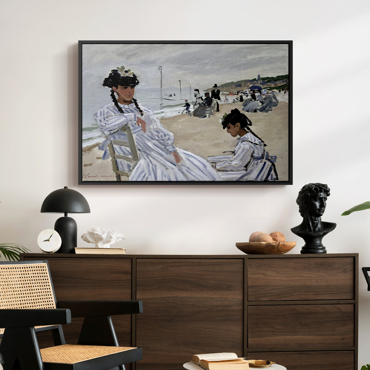 On the Beach at Trouville, 1870 by Claude Monet displayed in a black floater framed canvas above a dark wood credenza in an entryway.