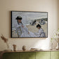 Black floater framed canvas of On the Beach at Trouville, 1870 by Claude Monet, featuring an impressionist seaside scene with women in dresses and hats above a sideboard in a softly lit hallway.