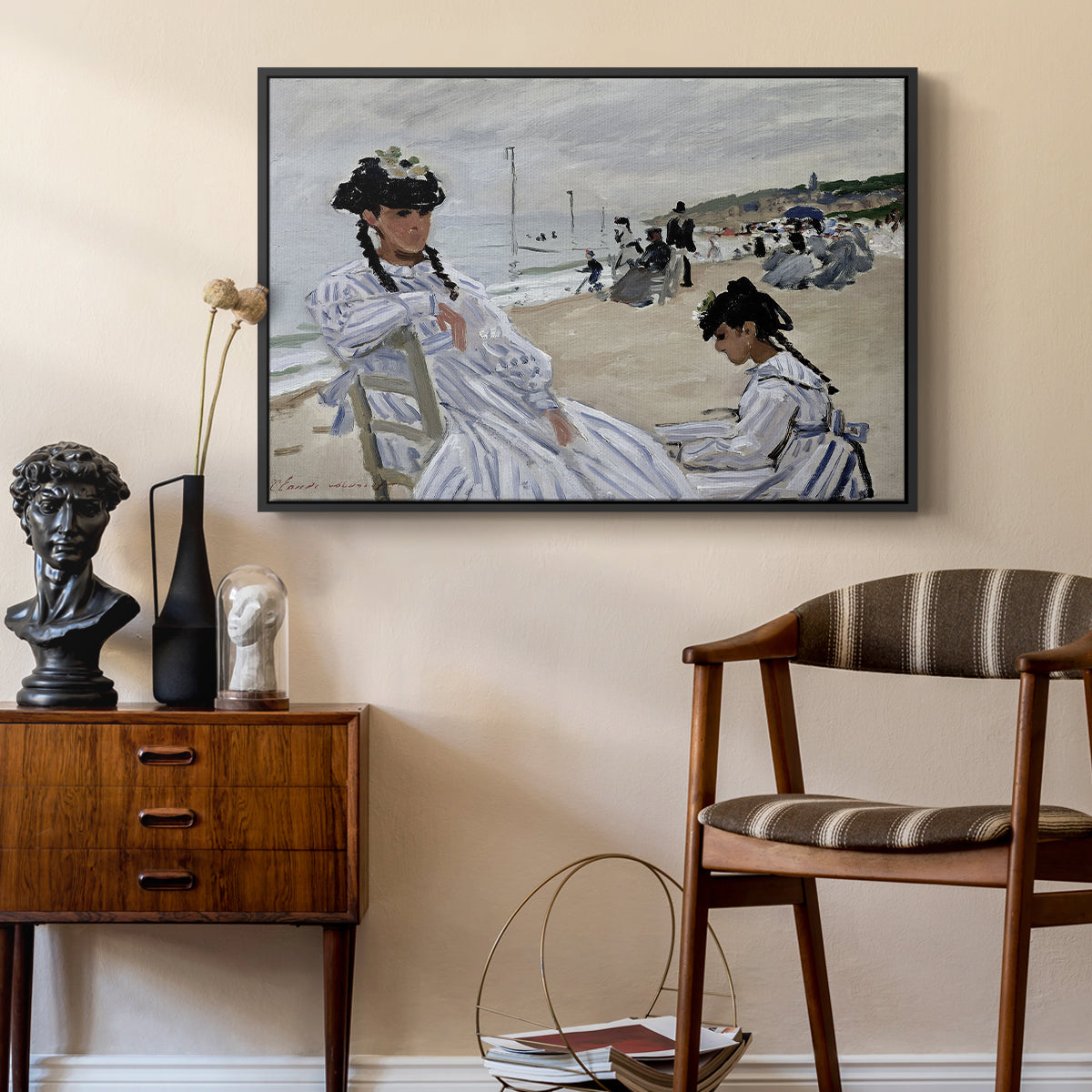 On the Beach at Trouville, 1870 by Claude Monet as a black floater framed canvas featuring a beach setting with people relaxing under umbrellas, styled above a mid-century console in a contemporary living area.