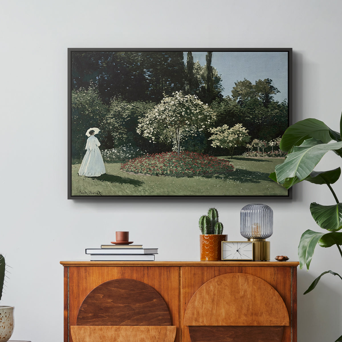 Woman in the Garden, Sainte-Adresse, 1867 by Claude Monet in a black floater framed canvas featuring a woman standing in garden surrounded by flowers and greenery, displayed above a wood console cabinet.