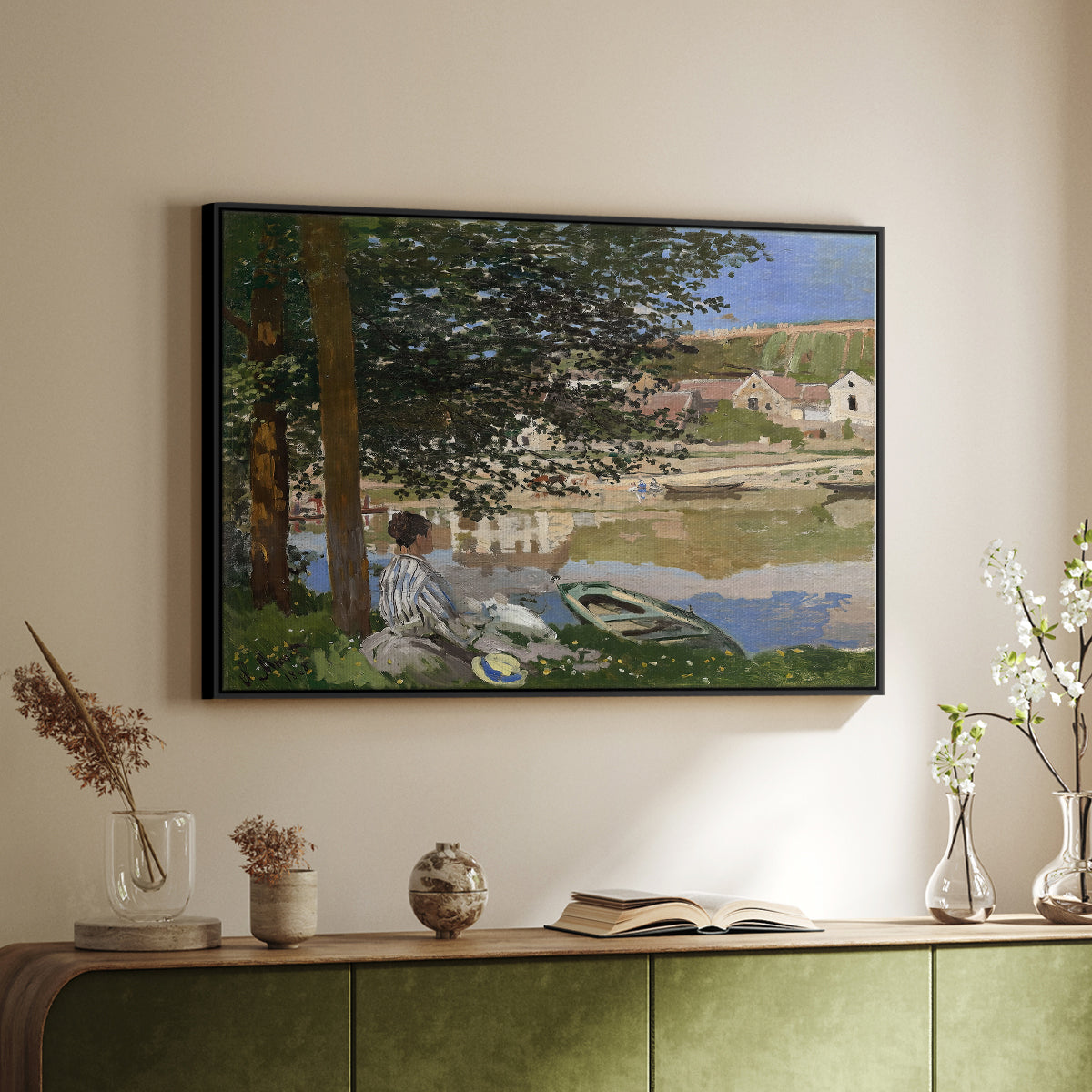 Black floater framed canvas of On the Bank of the Seine, Bennecourt, 1868 by Claude Monet, featuring a peaceful riverside scene with figures resting in grassy area by water above a sideboard in a softly lit hallway.