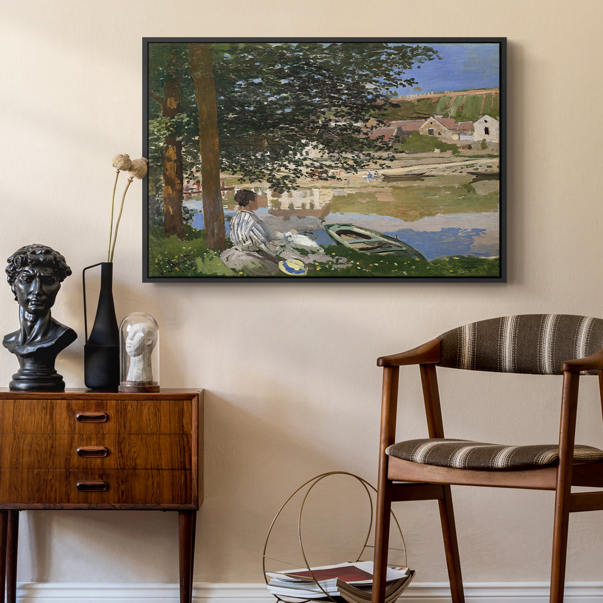 On the Bank of the Seine, Bennecourt, 1868 by Claude Monet as a black floater framed canvas featuring an impressionist landscape with people relaxing along the Seine, styled above a mid-century console in a contemporary living area.