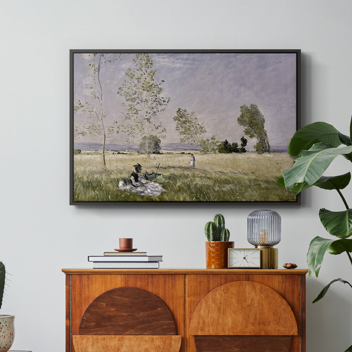 Summer (L'ete), 1874 by Claude Monet in a black floater framed canvas featuring a woman seated in grassy field beneath tree in bright summer landscape, displayed above a wood console cabinet.