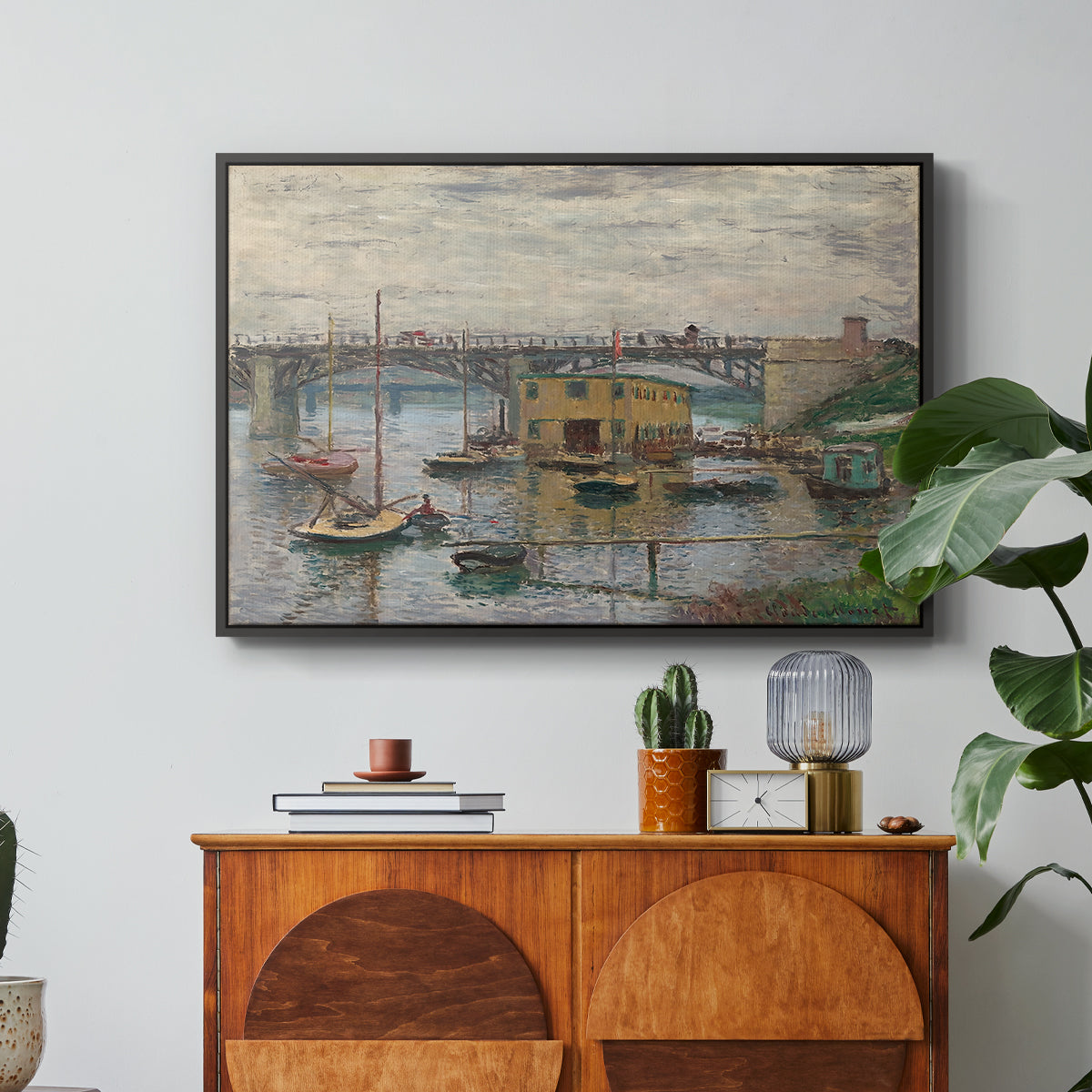 Bridge at Argenteuil on a Gray Day, c. 1876 by Claude Monet in a black floater framed canvas featuring a bridge crossing river under gray sky with muted reflections, displayed above a wood console cabinet.