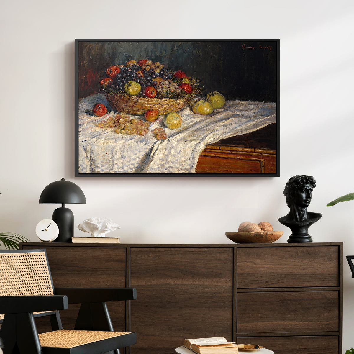 Still Life with Apples and Grapes, 1880 by Claude Monet displayed in a black floater framed canvas above a dark wood credenza in an entryway.