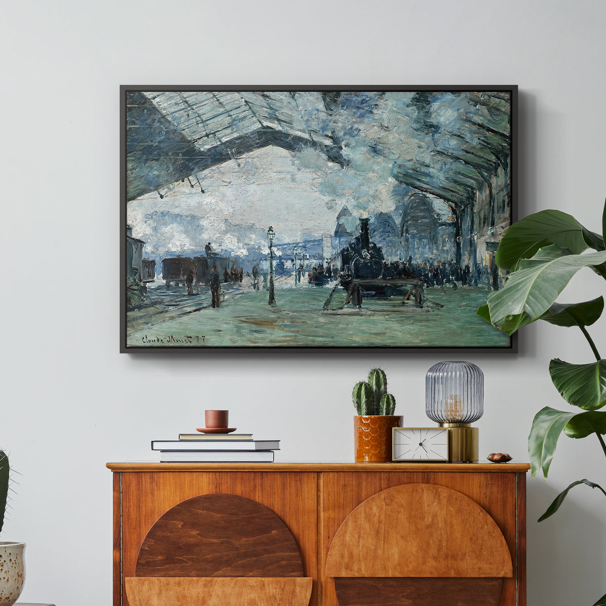 The Saint-Lazare Station, 1877 by Claude Monet in a black floater framed canvas featuring trains arriving under large arched station roof with billowing steam, displayed above a wood console cabinet.