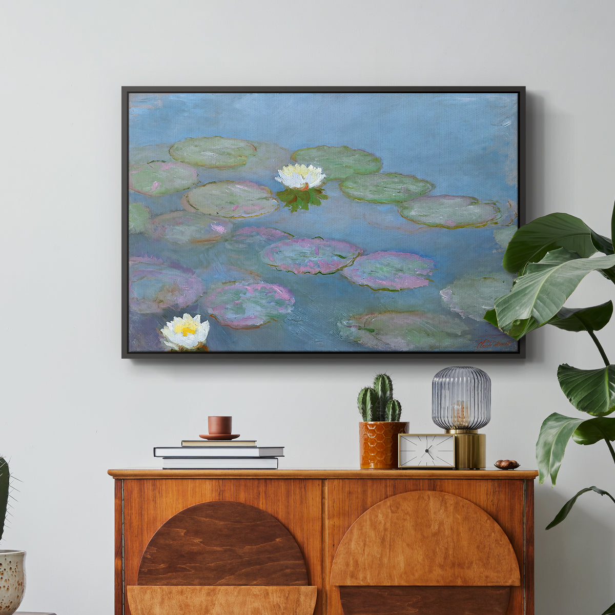 Water Lilies (Nymphéas), 1897-1899 by Claude Monet in a black floater framed canvas featuring floating water lilies on pond with reflections of sky and foliage, displayed above a wood console cabinet.
