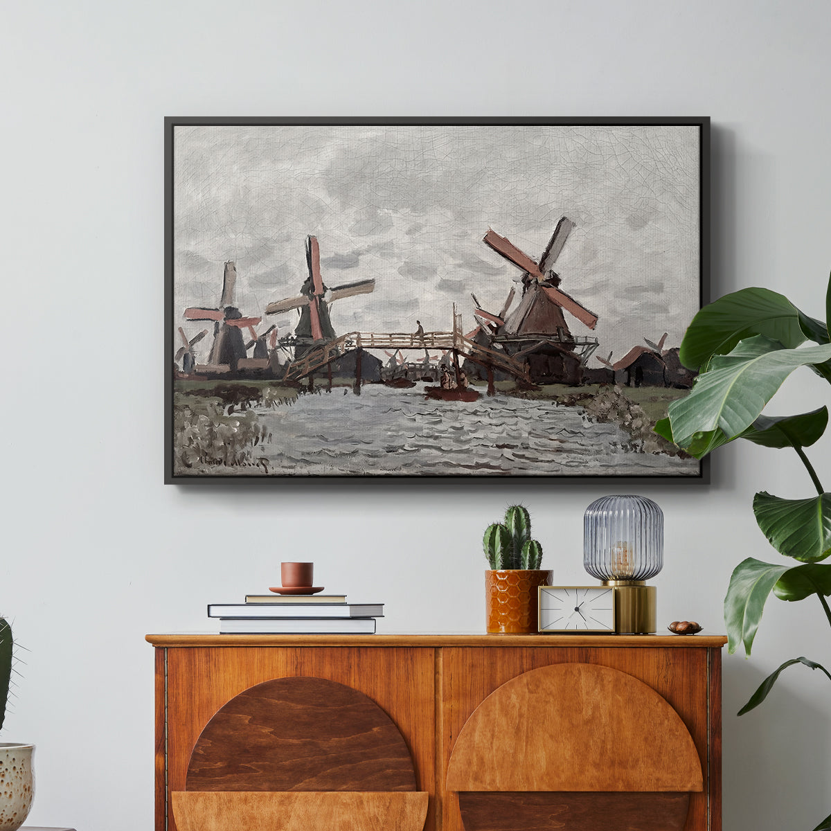 Windmills near Zaandam, 1871 by Claude Monet in a black floater framed canvas featuring windmills standing beside water under open sky in rural landscape, displayed above a wood console cabinet.