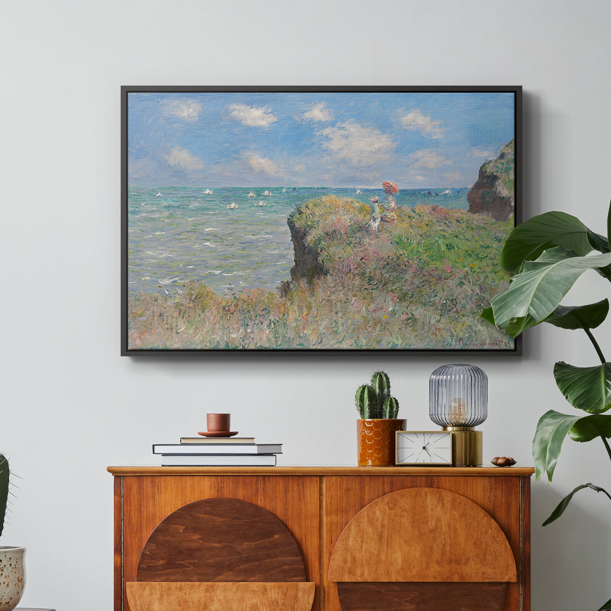 The Cliff Walk at Pourville, 1882 by Claude Monet in a black floater framed canvas featuring figures walking along coastal cliff path overlooking ocean and sky, displayed above a wood console cabinet.