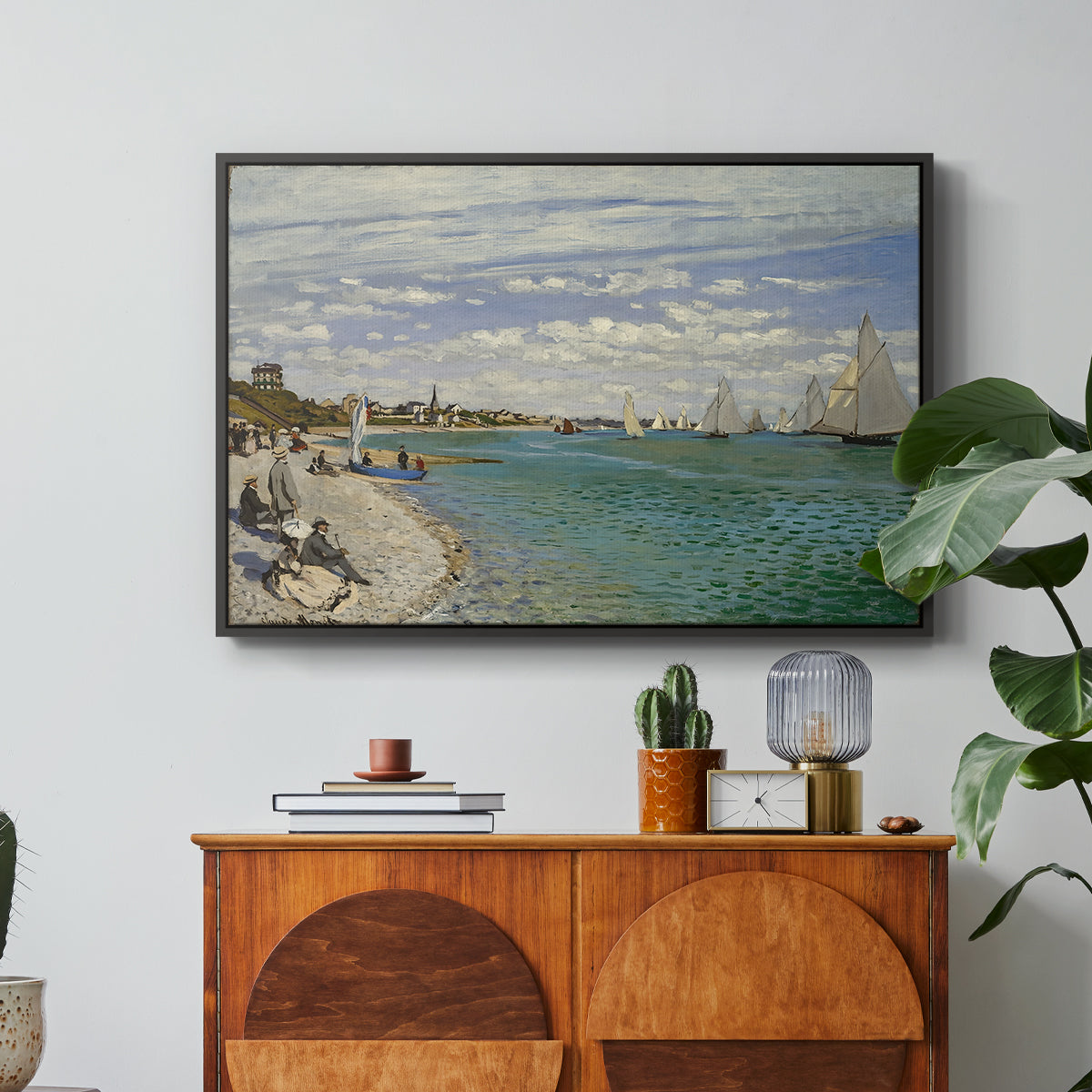 Regatta at Sainte-Adresse, 1867 by Claude Monet in a black floater framed canvas featuring sailboats gathered near shore with flags and spectators along coastline, displayed above a wood console cabinet.