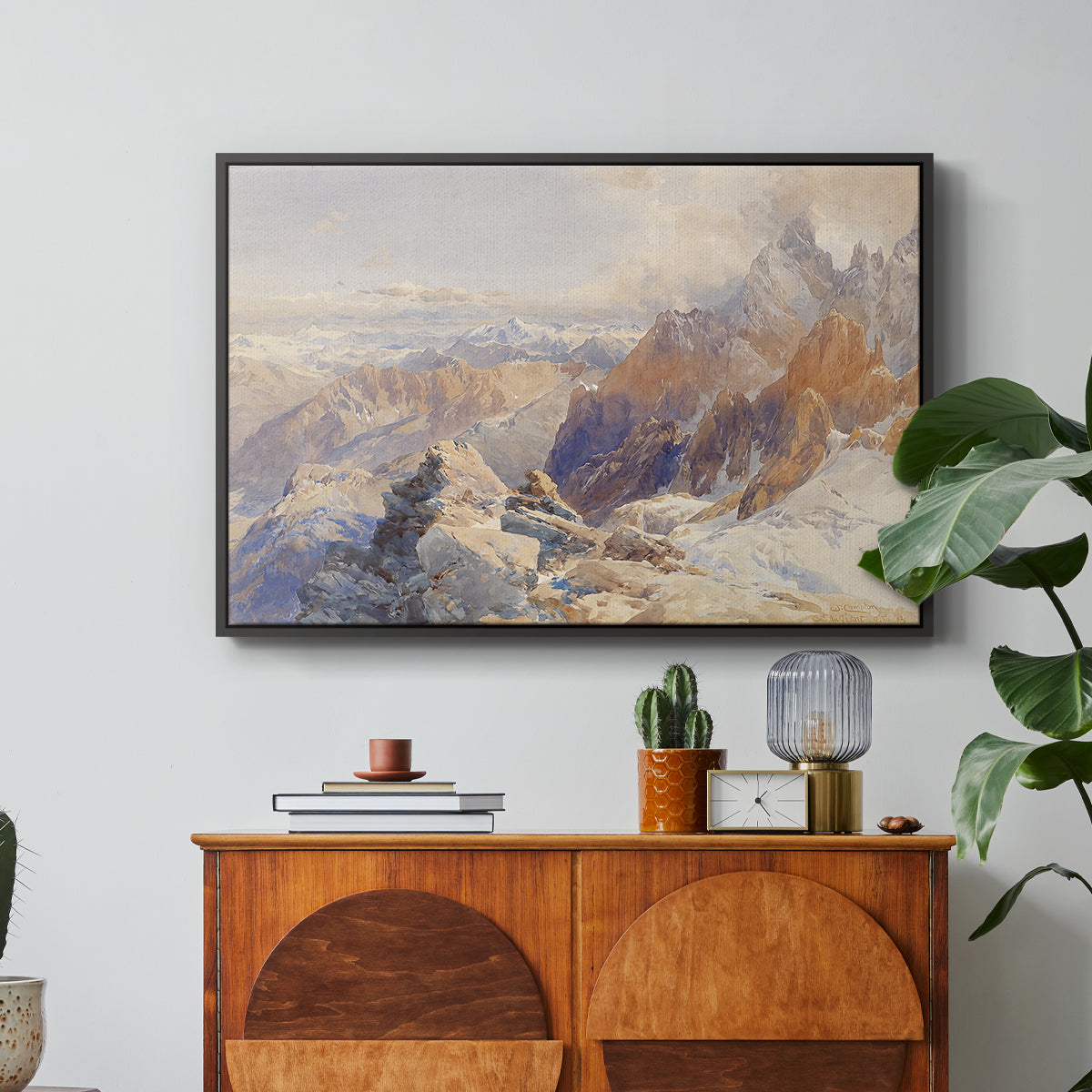 Col du Géant, 1903 by Edward Theodore Compton in a black floater framed canvas featuring a mountain pass with snow-covered peaks and expansive alpine valley, displayed above a wood console cabinet.