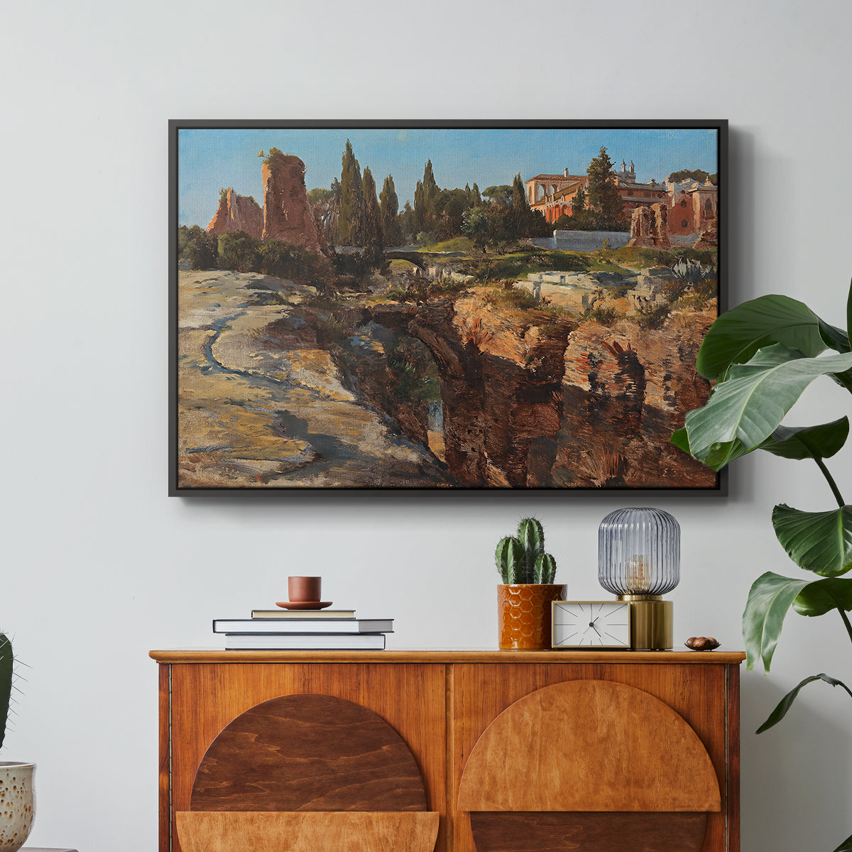 Palatine in Rome, c. 1921 by Edward Theodore Compton in a black floater framed canvas featuring historic Roman ruins and buildings set within warm landscape, displayed above a wood console cabinet.