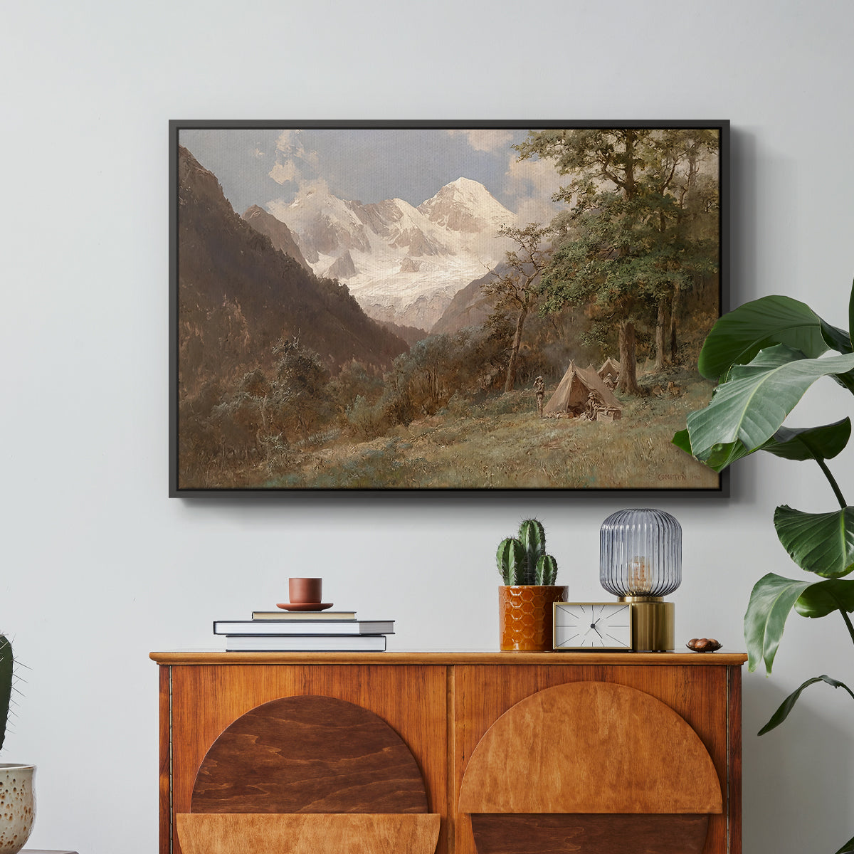 Landscape in the Caucasus, c. 1921 by Edward Theodore Compton in a black floater framed canvas featuring a mountainous landscape with rugged terrain and distant peaks, displayed above a wood console cabinet.