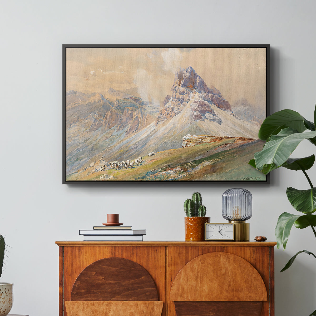 From the Dolomites, 1904 by Edward Theodore Compton in a black floater framed canvas featuring dramatic Dolomite mountain peaks rising above rugged terrain, displayed above a wood console cabinet.