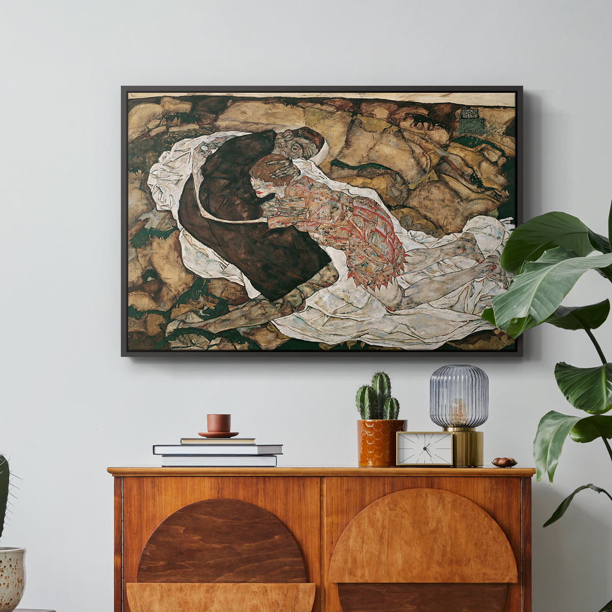 Death and the Maiden, 1915 by Egon Schiele in a black floater framed canvas featuring intertwined figures representing death and woman in emotional embrace, displayed above a wood console cabinet.
