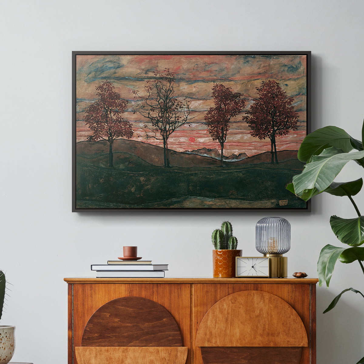 Four Trees, 1917 by Egon Schiele in a black floater framed canvas featuring four trees standing in open landscape against colorful sky, displayed above a wood console cabinet.
