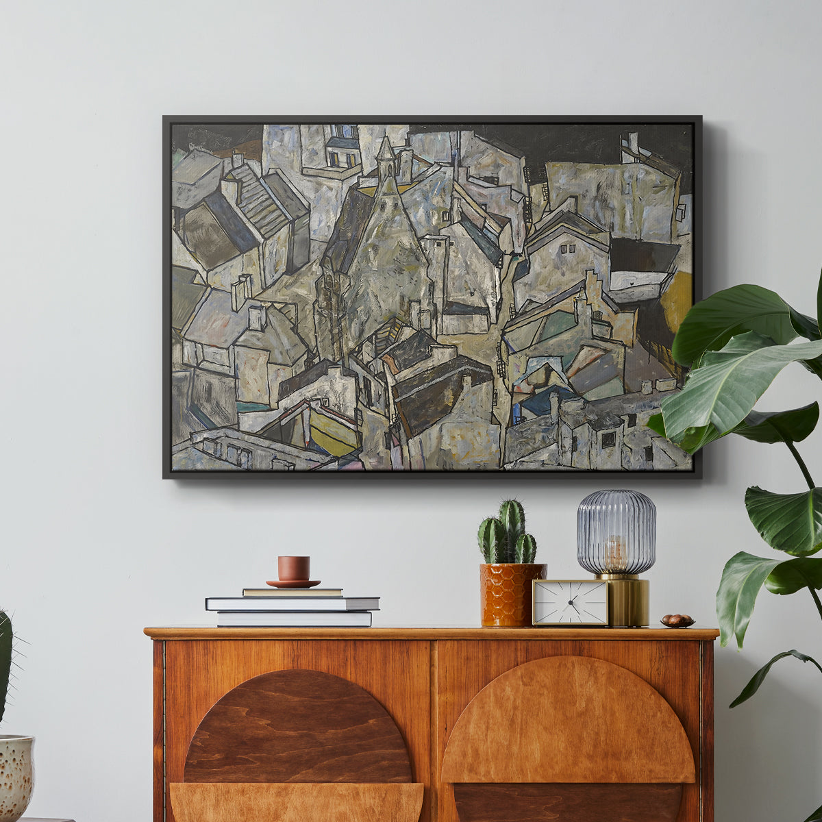 Mödling II, 1918 by Egon Schiele in a black floater framed canvas featuring clustered geometric houses forming dense urban landscape with sharp angles, displayed above a wood console cabinet.