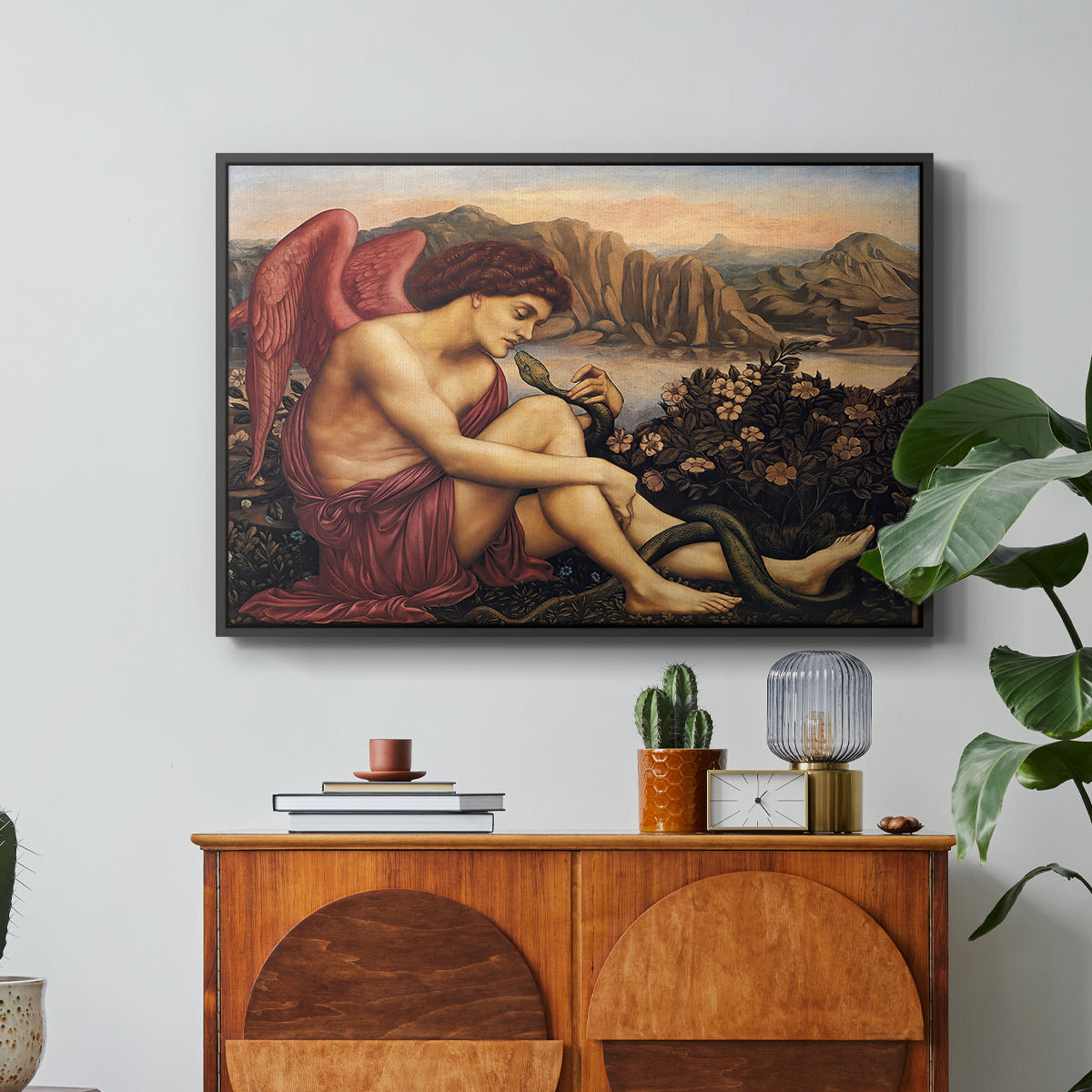 The Angel with the Serpent, c. 1870-1875 by Evelyn De Morgan in a black floater framed canvas featuring an angelic figure confronting serpent in symbolic battle of good and evil, displayed above a wood console cabinet.