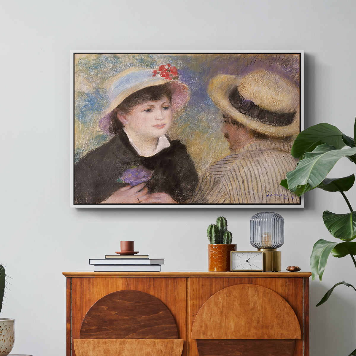 Boating Couple (Aline Charigot and Renoir), c. 1881 by Pierre-Auguste Renoir in a white floater framed canvas featuring a close-up of a couple seated together outdoors with hats and soft sunlight, displayed above a wood console cabinet.