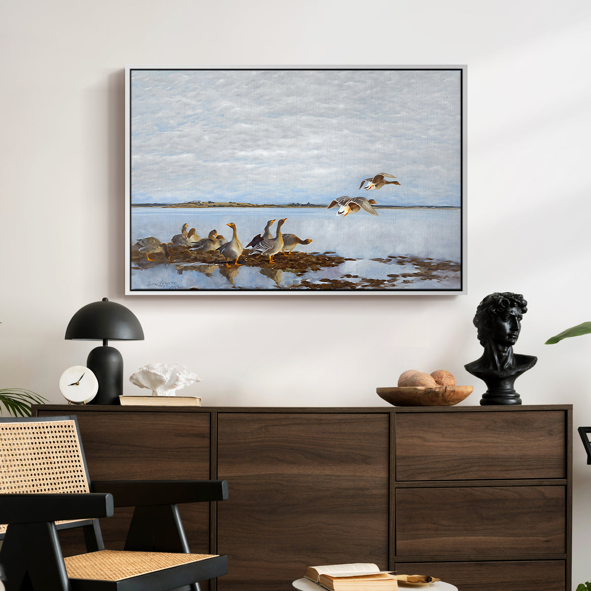 Greylag Geese (Grågäss), 1922 by Bruno Liljefors displayed in a white floater framed canvas above a dark wood credenza in an entryway.