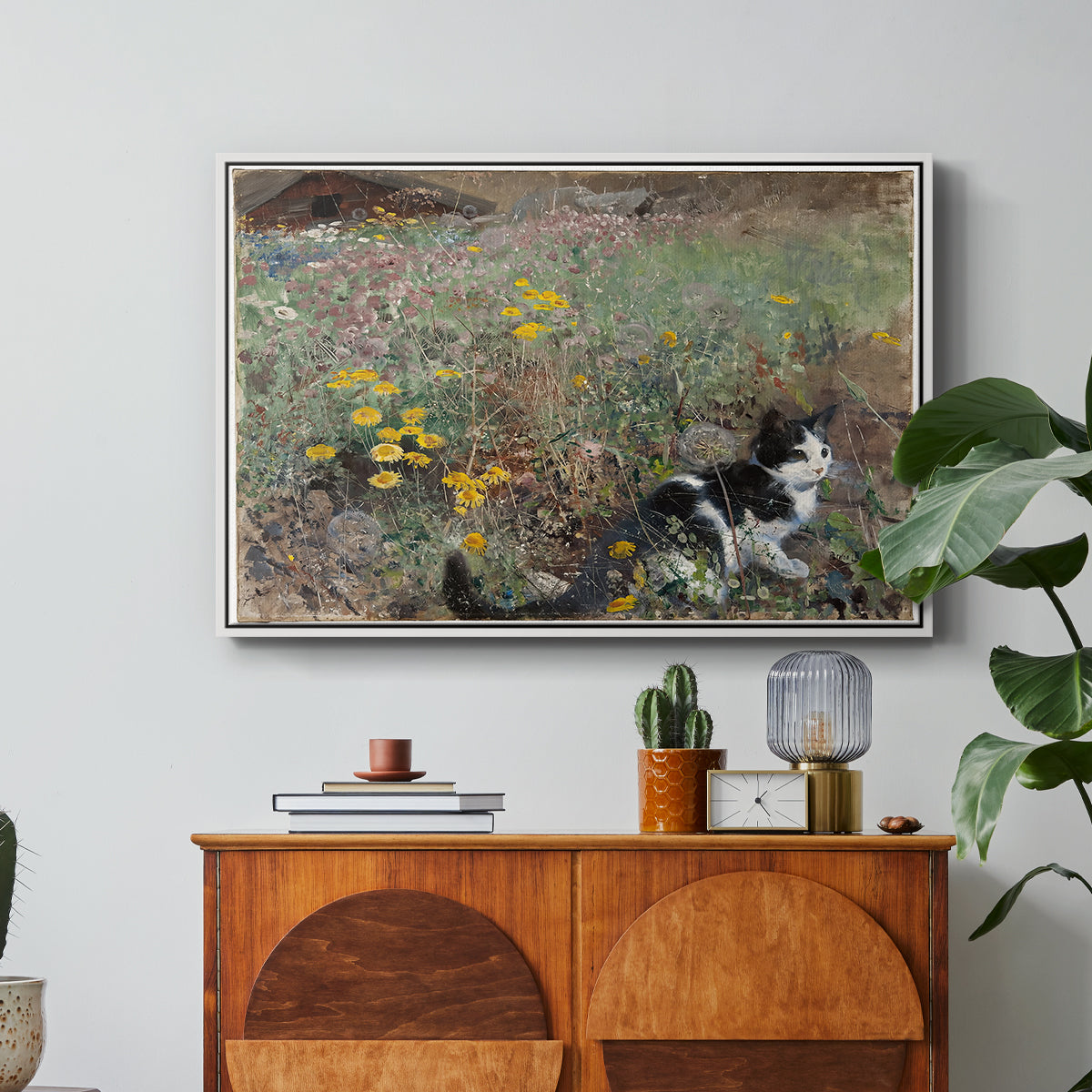 Cat on a Flowery Meadow, 1887 by Bruno Liljefors in a white floater framed canvas featuring a cat crouching in a meadow filled with wildflowers and greenery, displayed above a wood console cabinet.