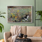 White floater framed canvas featuring a naturalistic depiction of cat in blooming countryside setting, displayed above a sofa in a modern living room.