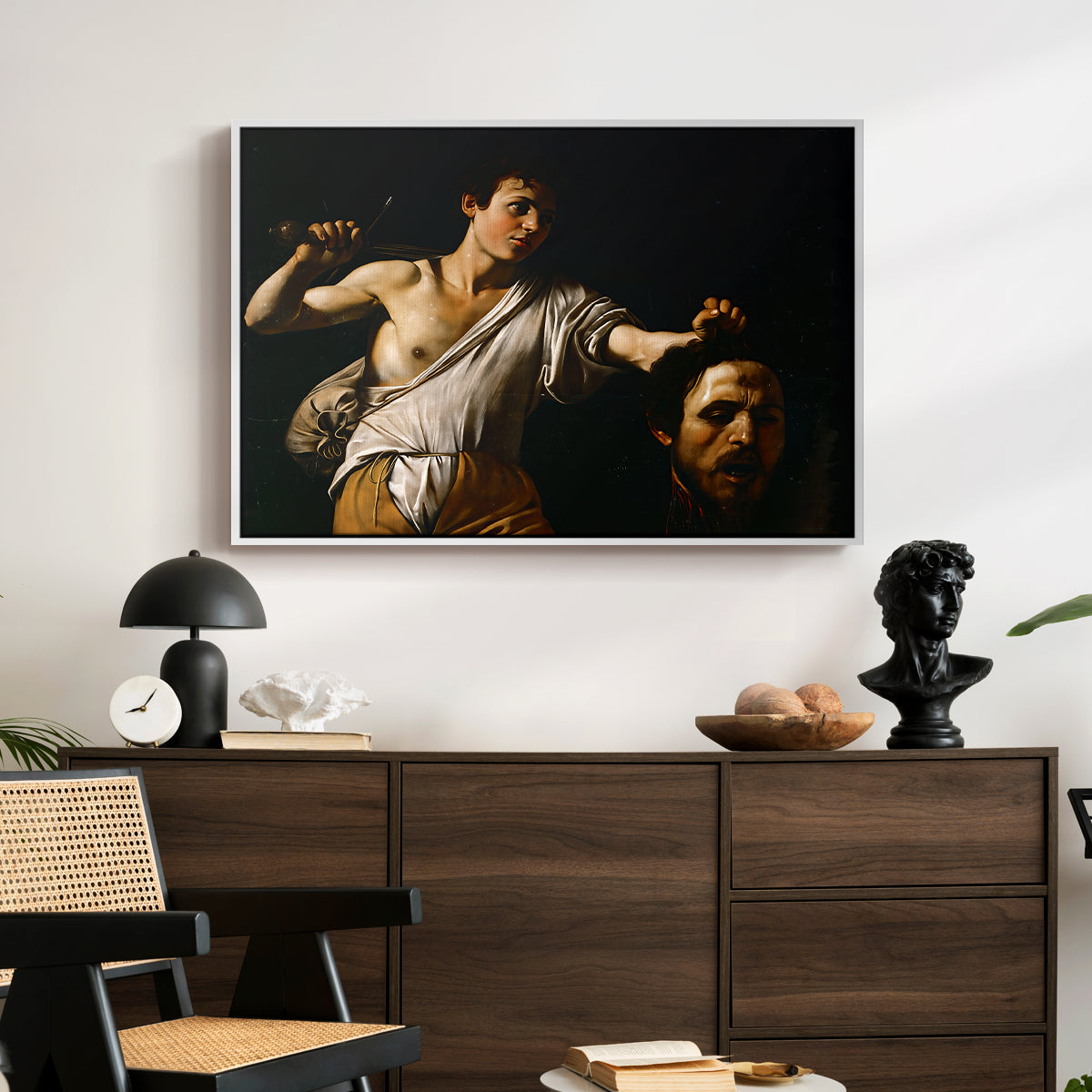 David with the Head of Goliath (Vienna Version), c. 1607 by Caravaggio displayed in a white floater framed canvas above a dark wood credenza in an entryway.