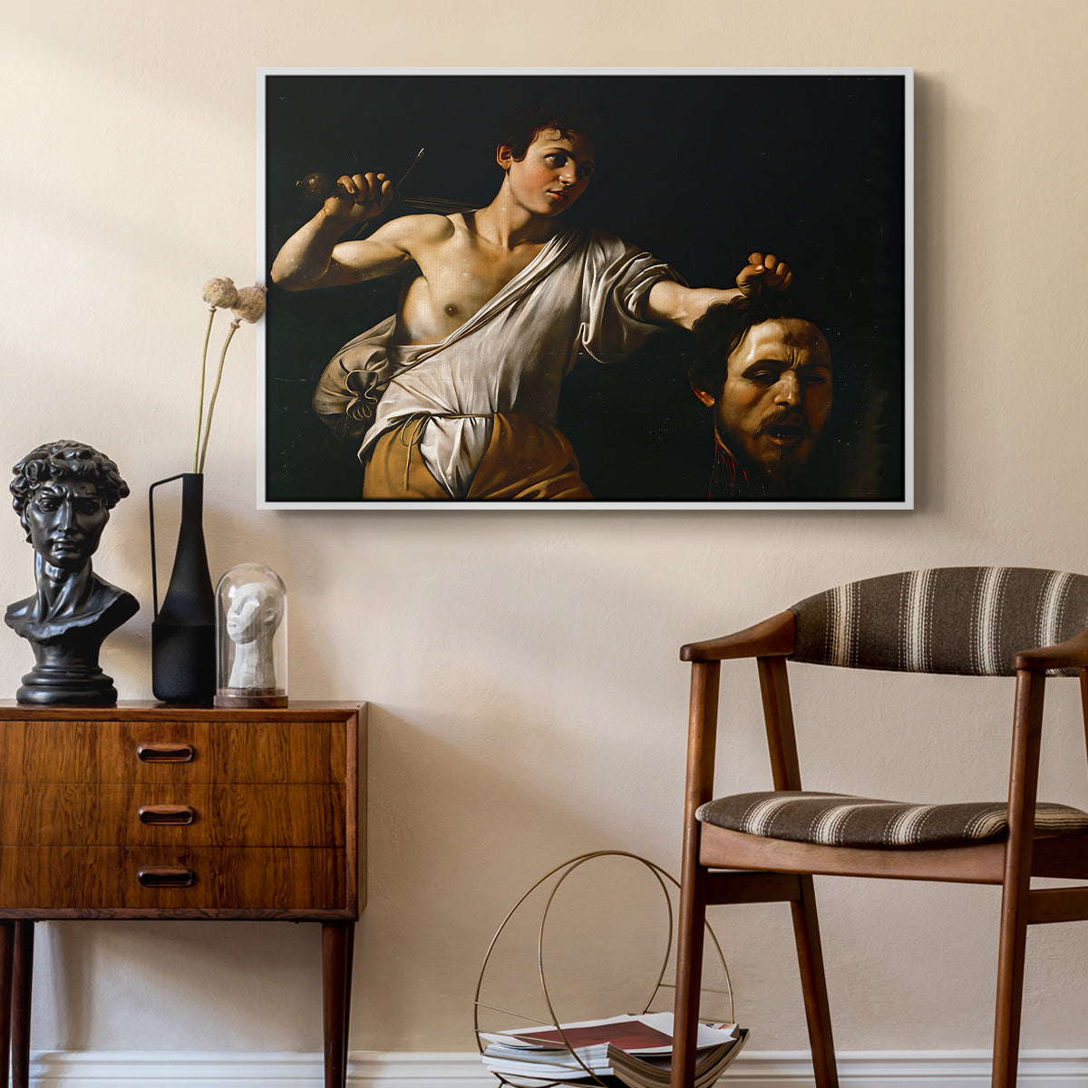 David with the Head of Goliath (Vienna Version), c. 1607 by Caravaggio as a white floater framed canvas featuring a Baroque depiction of youth holding severed head in shadowy setting, styled above a mid-century console in a contemporary living area.