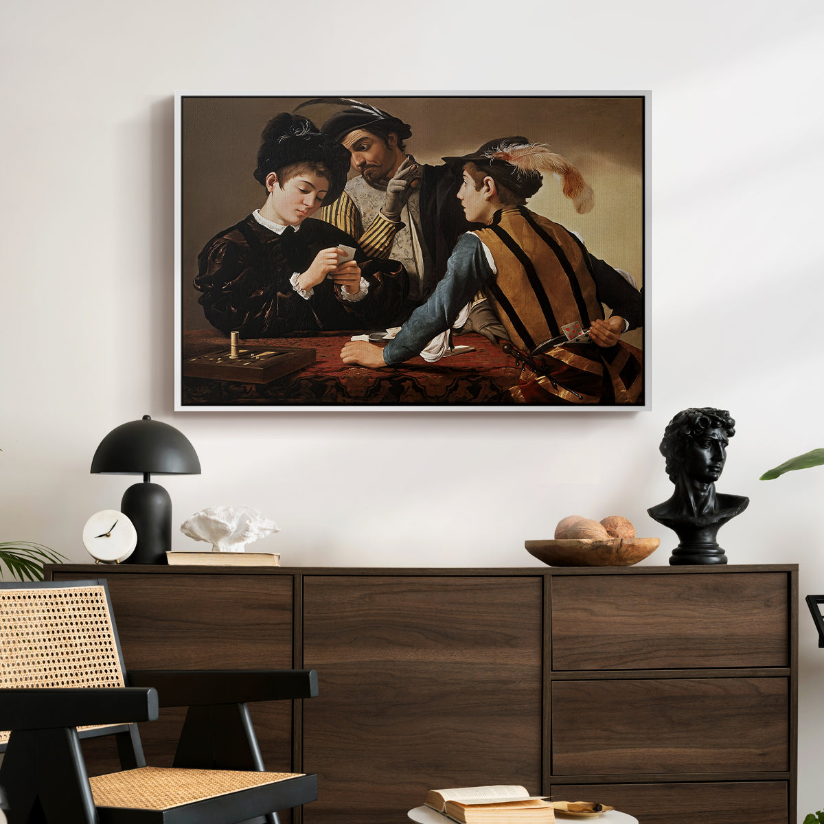 The Cardsharps, c. 1594 by Caravaggio displayed in a white floater framed canvas above a dark wood credenza in an entryway.