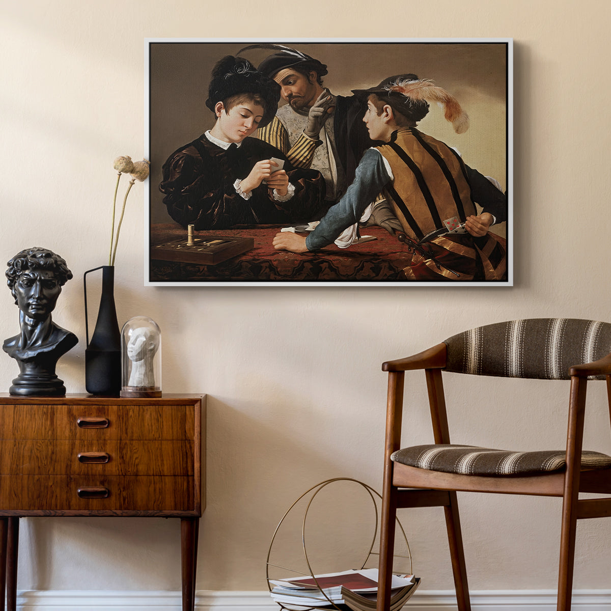 The Cardsharps, c. 1594 by Caravaggio as a white floater framed canvas featuring a young men playing cards with one cheating and another watching closely, styled above a mid-century console in a contemporary living area.