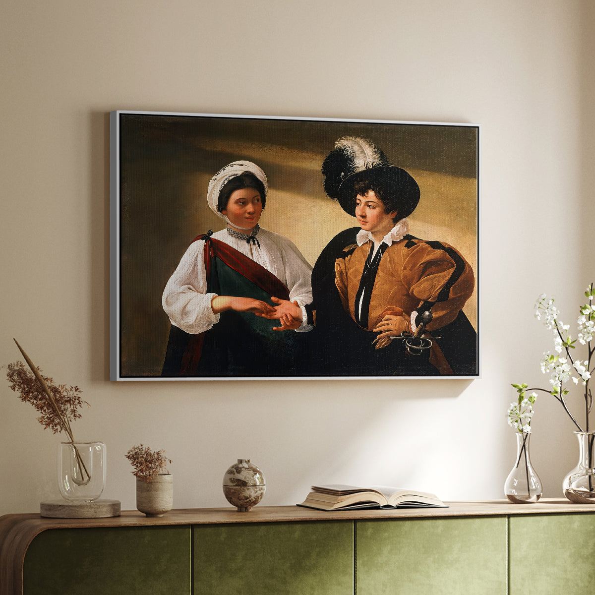 White floater framed canvas of The Fortune Teller (Louvre Version), c. 1595 by Caravaggio, featuring a fortune teller examining hand of man as she slyly removes his ring above a sideboard in a softly lit hallway.