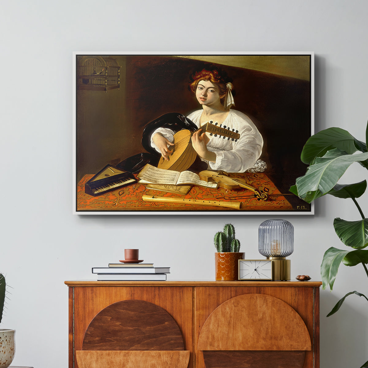 The Lute Player (Wildenstein Version), c. 1596 by Caravaggio in a white floater framed canvas featuring a young man playing lute surrounded by sheet music and still life objects, displayed above a wood console cabinet.