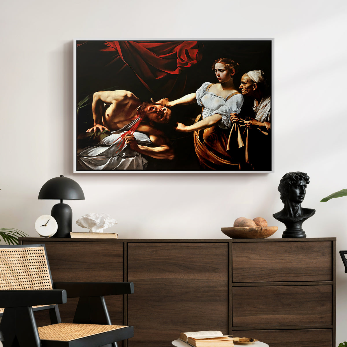 Judith Beheading Holofernes, c. 1599 by Caravaggio displayed in a white floater framed canvas above a dark wood credenza in an entryway.