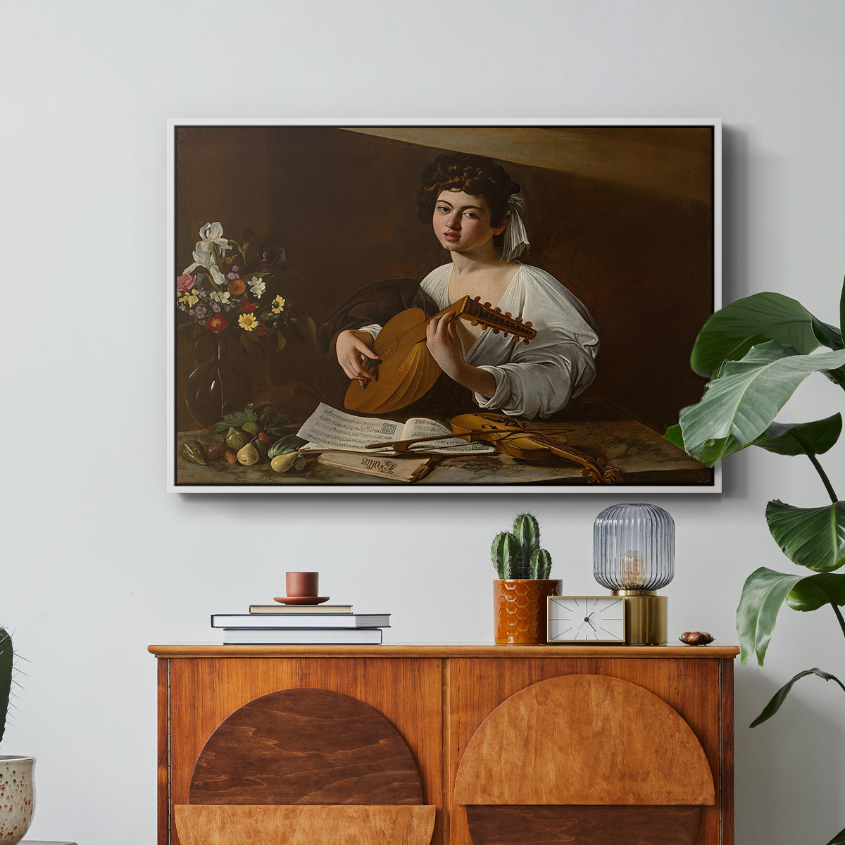 The Lute Player (Hermitage Version), c. 1596 by Caravaggio in a white floater framed canvas featuring a young musician playing lute beside table with fruit and sheet music, displayed above a wood console cabinet.