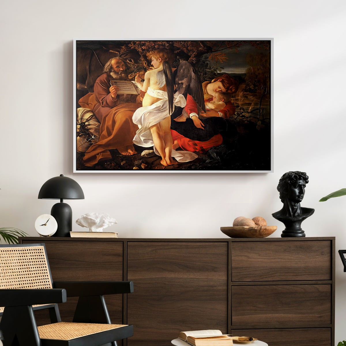 Rest on the Flight into Egypt, c. 1597 by Caravaggio displayed in a white floater framed canvas above a dark wood credenza in an entryway.