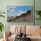 White floater framed canvas featuring a coastal landscape with boats and people along shore, displayed above a sofa in a modern living room.