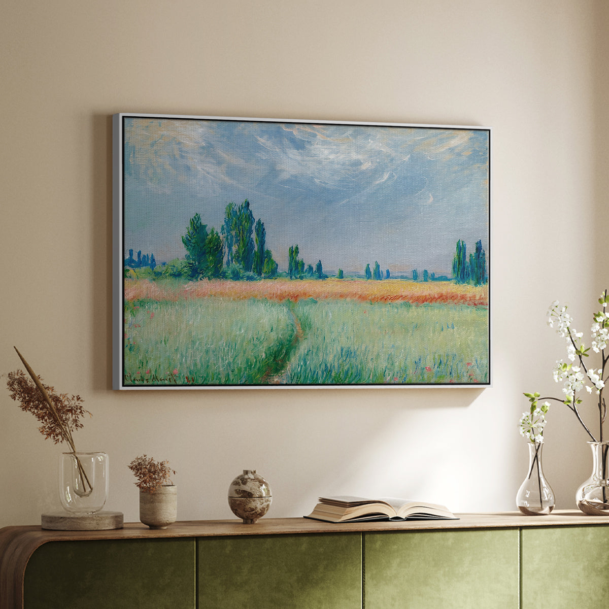 White floater framed canvas of The Wheat Field (Champ de Blé), 1881 by Claude Monet, featuring an impressionist depiction of ripened grain field in countryside above a sideboard in a softly lit hallway.