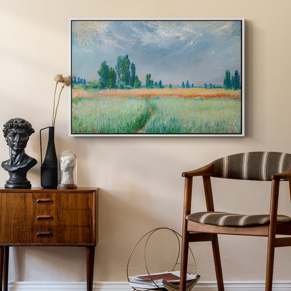 The Wheat Field (Champ de Blé), 1881 by Claude Monet as a white floater framed canvas featuring an agricultural landscape with tall wheat and distant horizon, styled above a mid-century console in a contemporary living area.